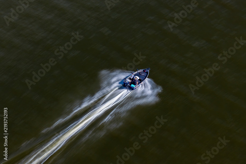 Aerial view of a fast fishing motor boat creating a white wake on dark water, Poland.