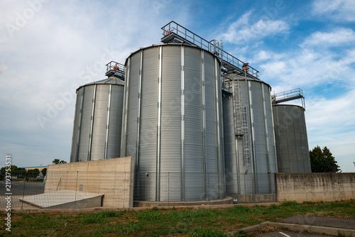 Grain storage silos at agricultural facility, metal cereal silos for wheat and corn, modern farming infrastructure, agribusiness logistics, food supply chain, harvest storage, industrial agriculture.
