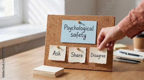 A person pinning a note labeled disagree to a cork board with notes about psychological safety, including ask and share