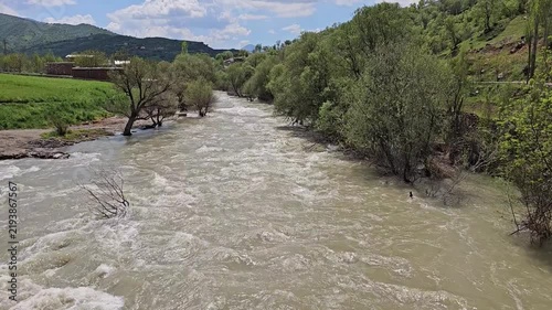 Swift, foaming river winds through a lush green valley, bordered by orchards, dense trees, and an open meadow under a partly cloudy sky.
📍 Dorud, Sarvabad, Kurdistan 
