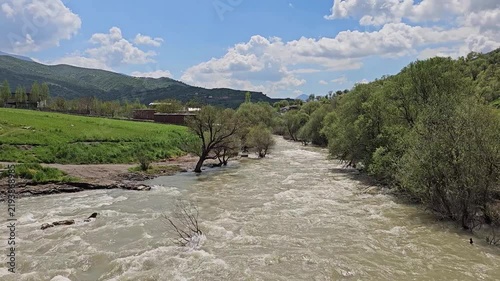 Swift, foaming river winds through a lush green valley, bordered by orchards, dense trees, and an open meadow under a partly cloudy sky.
📍 Dorud, Sarvabad, Kurdistan 