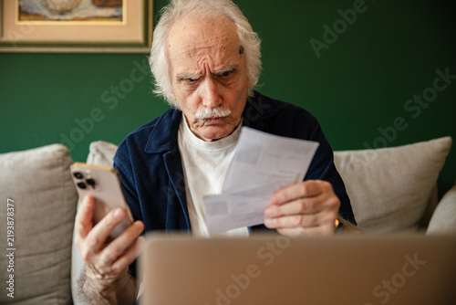 Senior man worried about bills while checking smartphone at home