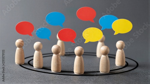 Wooden figures surround colorful speech bubbles, symbolizing communication and discussion.