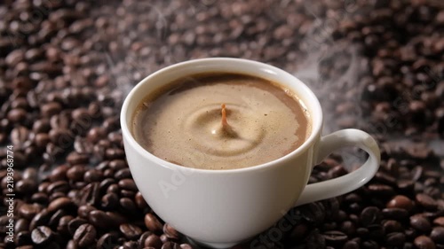 Close-up of hot coffee with a foamy surface and gentle ripples, served in a white cup surrounded by roasted coffee beans for food and beverage advertising.