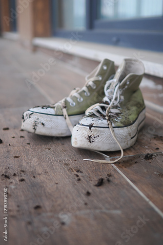 Fotografie Old sneakers on a wooden floor with dirt scattered around