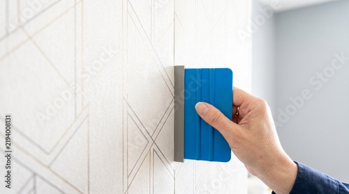 Hand using smoothing tool to precisely install patterned wallpaper, ensuring perfect pattern matching