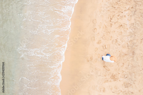 Aerial top-down view of woman in a hat walking along the beach near the sea waves.