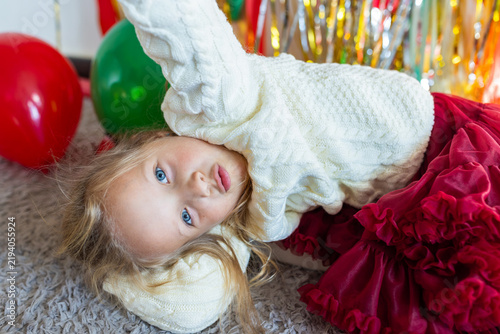 Young girl in white sweater and red skirt lying on carpet at festive party