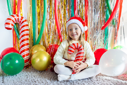 Young girl wearing Santa hat holding candy cane balloon at festive holiday party