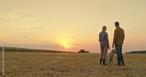 Farmers with Dog in Harvested Field at Sunset
