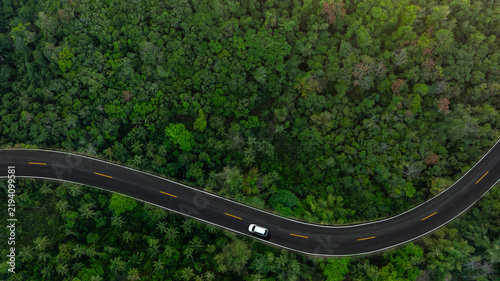 Aerial view of dark green forest road and white electric car Natural landscape and elevated roads Adventure travel and transportation and environmental protection concept	
