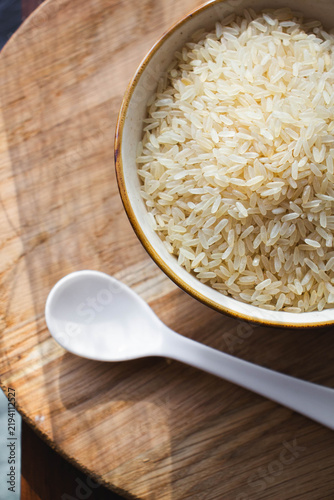 Uncooked White Rice in Ceramic Bowl with Spoon on Wooden Table