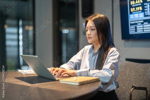 Smiling Asian business woman using laptop in modern digital workplace, Female corporate worker analyzing data technology in office, Financial management, software dashboards and tech startup concepts
