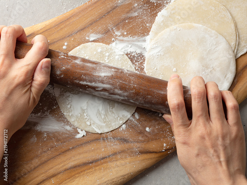 Hands rolling out dumpling dough wrapper with wooden rolling pin