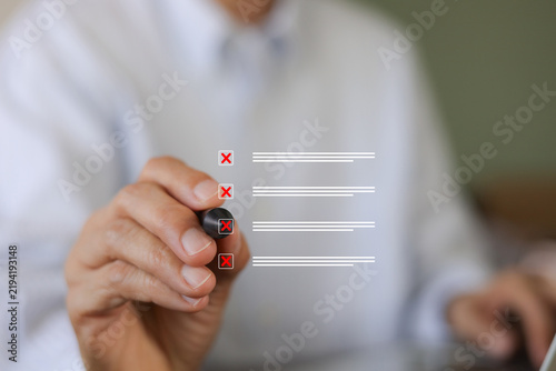 A businessman holds a marker to check red cross mark rejection symbols on a digital virtual checklist, illustrating failure, error verification, quality control, survey feedback, and wrong decisions.