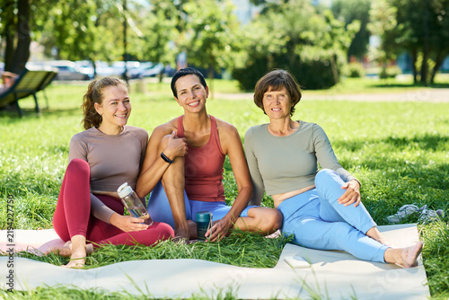 Portrait of young adult and middle aged Caucasian women sitting on exercise mats in park resting after fitness workout. Imagery suitable for wellness apps, healthy lifestyle campaigns