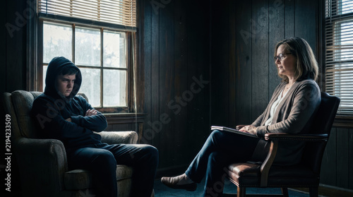 Male teenager therapy chair counseling session therapist defiant expression wood paneled room