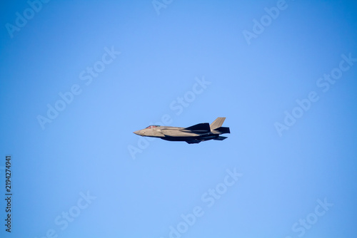 F-35A Lightning II fighter aircraft flying across a blue sky, photographed in side profile showing its distinctive stealth aircraft design.