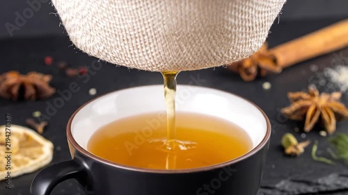 Herbal tea straining into a dark ceramic cup.