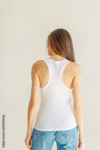 Fotografie Model stands with back to camera in plain white cotton tank top, mockup shown from back for full catalog, space left for print