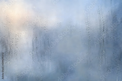 Blue frosted wet glass surface with soft condensation and blurred cool shapes behind the window.