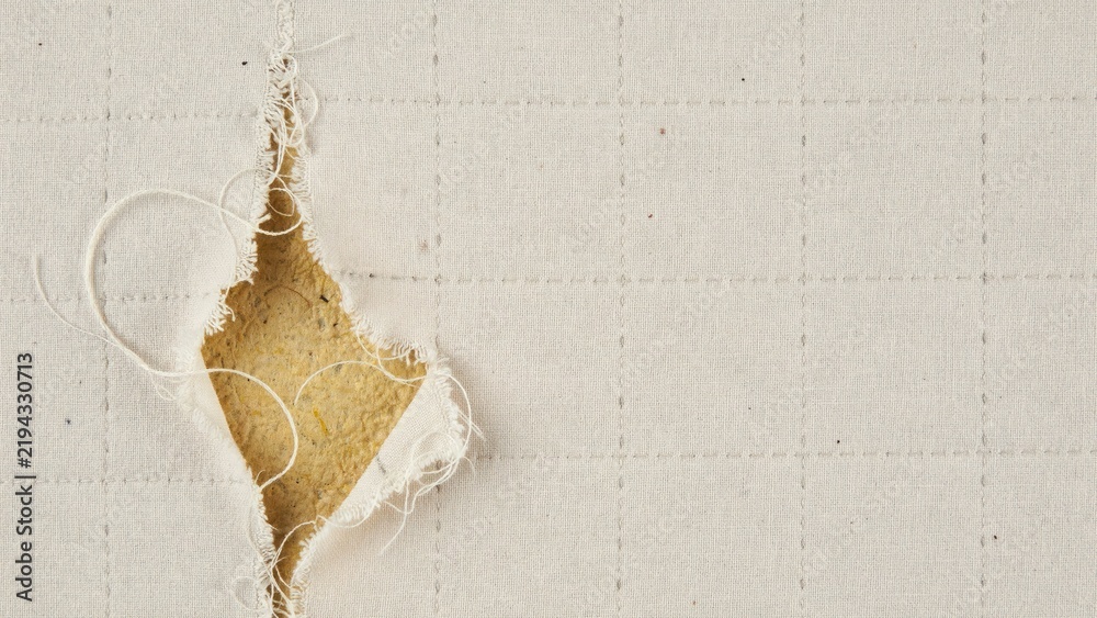 Obraz premium Close-up of torn off-white quilted fabric revealing yellow foam underlay