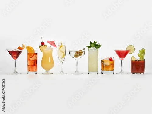 Row of eight assorted cocktails with garnishes on white background