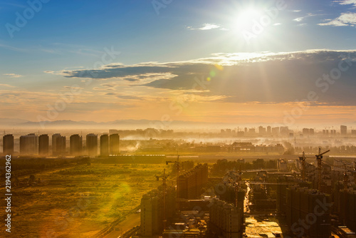 фотографія A misty urban landscape at sunrise, showing ongoing construction and distant city buildings under a bright sky