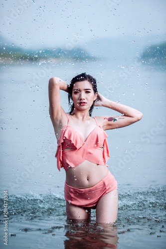 Joyful Asian woman cooling off in natural water splash during summer vacation, enjoying refreshed freedom.