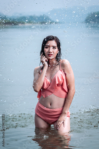 Joyful Asian woman cooling off in natural water splash during summer vacation, enjoying refreshed freedom.
