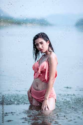 Joyful Asian woman cooling off in natural water splash during summer vacation, enjoying refreshed freedom.