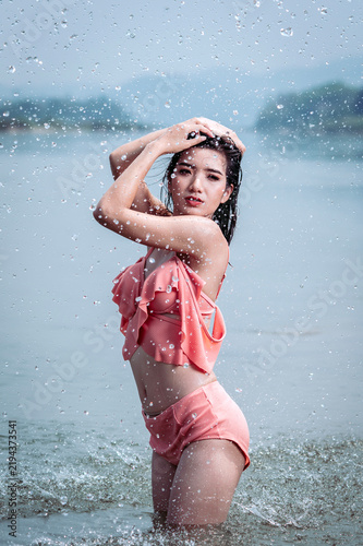 Joyful Asian woman cooling off in natural water splash during summer vacation, enjoying refreshed freedom.