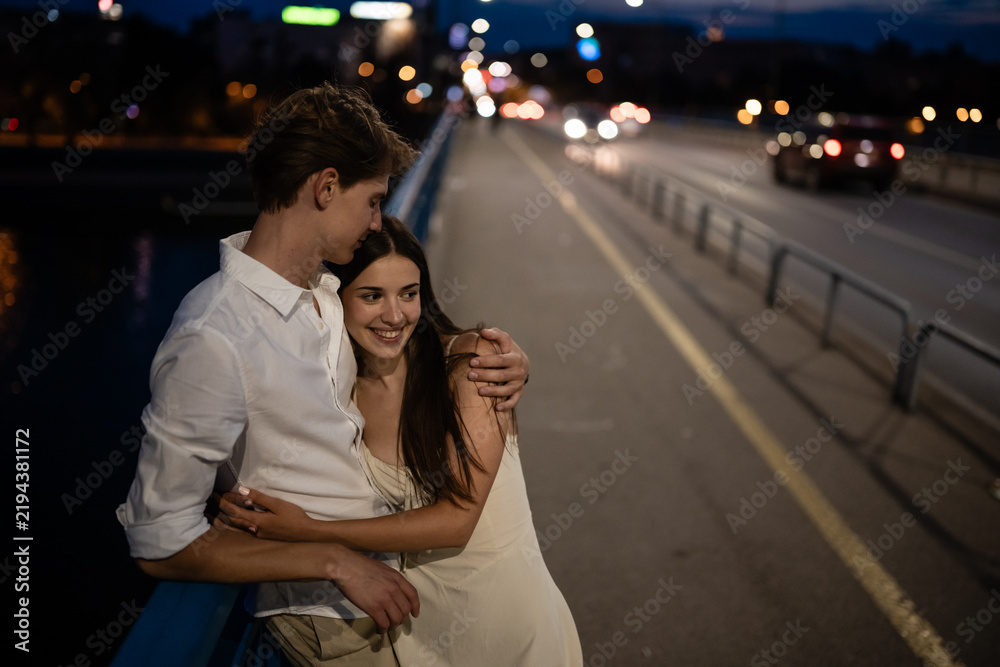 Fototapeta premium Young couple embracing on urban bridge at night
