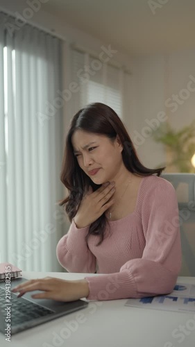 Sick asian businesswoman coughing while working on laptop at home office