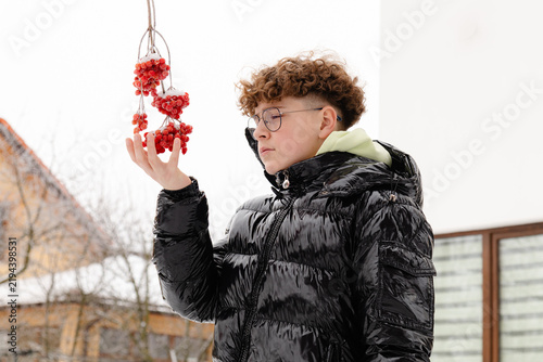 Принти на полотні Boy holds red viburnum berries in his hand in a snowy setting during winter