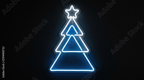 Glowing blue and white neon Christmas tree sign with star topper on dark background