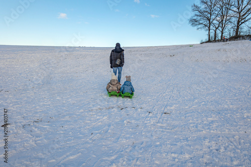 Foto Father pulling two little daughters on green plastic sled across snowy winter fi