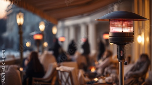 close up of a sleek modern infrared patio heater glowing softly above a covered winter terrace, softly blurred background showing people wrapped