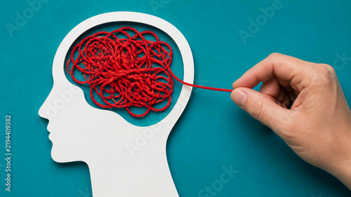A hand pulls a red thread out of a tangled mess inside a white head silhouette on a blue background.