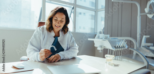 Female dentist examines clear aligner at desk in dental clinic
