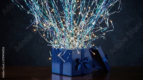 Blue gift box unboxing with glowing tinsel and party lights exploding out. Festive holiday surprise kit on a dark wooden table background.