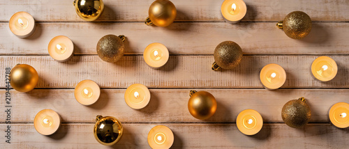 overhead flat lay view of golden christmas baubles and burning tealight candles arranged on rustic white wooden background forming seasonal holiday celebration border design pattern