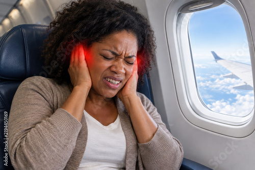 An African American woman sitting by the window experiences severe ear pain during the takeoff of a passenger plane. The area of pain is highlighted in red.