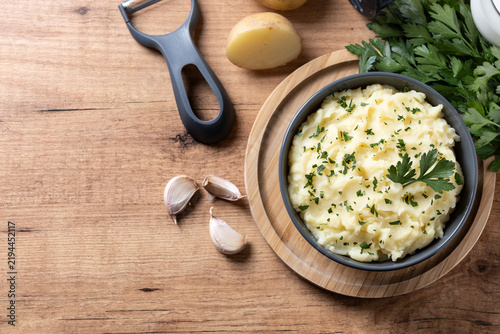 Creamy mashed potatoes with parsley and fresh ingredients on wooden table. Top view. Copy space