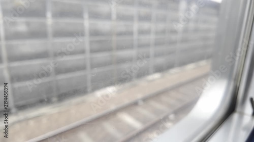 Passenger view looking out of a moving train window at tracks and sound barrier walls.