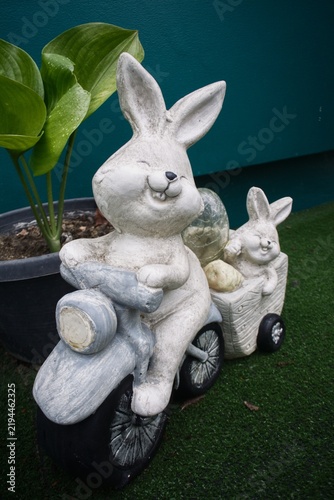 Foto ​Cute stone rabbit riding scooter statue with baby bunny passenger in garden dec
