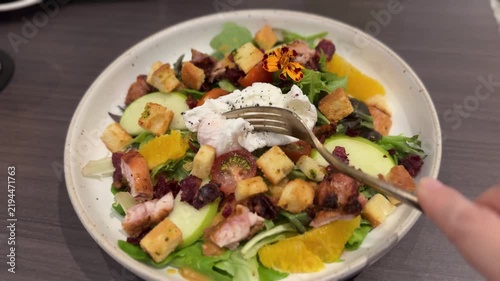 Fork Breaking Runny Poached Egg on Fresh Mixed Salad.

