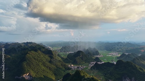 Landscape view: Rain shaft descending over a rural valley with a village at the foot of karst hills