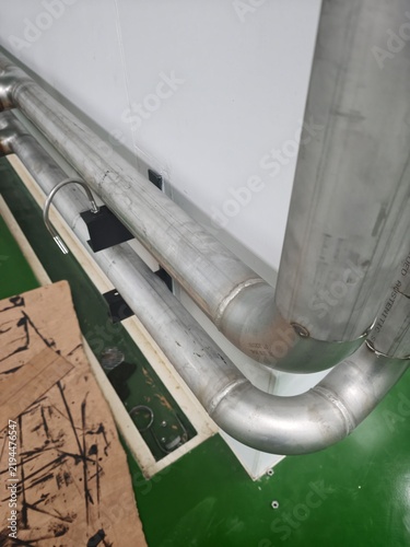 An interior shot of stainless steel process piping mounted along clean white sandwich panel walls in an industrial cleanroom facility, featuring heavy-duty wall brackets, precision bends, and scaffold