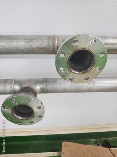 A close-up shot of a precision-welded stainless steel pipe flange with bolt holes, installed on an industrial process pipeline against cleanroom walls and epoxy flooring.